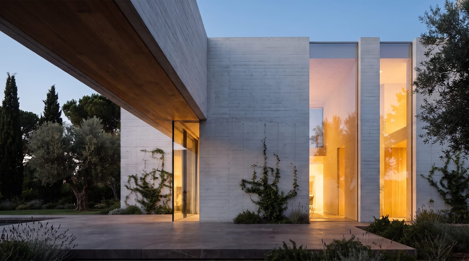 A contemporary concrete house at dusk, warm light in deep openings